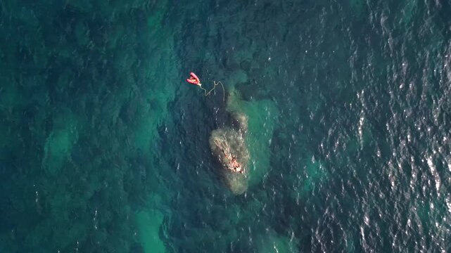Aerial view of a swimmer with a red safety buoy in the clear turquoise waters of Cala Llebeig, El Poble Nou de Benitatxell, Valencian Community, Spain.