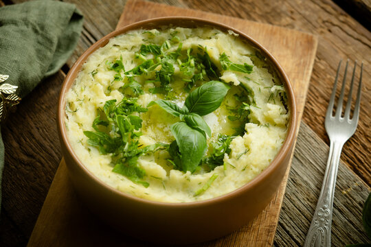 Bowl of mashed potatoes adorned with butter and herbs on rustic wooden table. Thanksgiving meal.