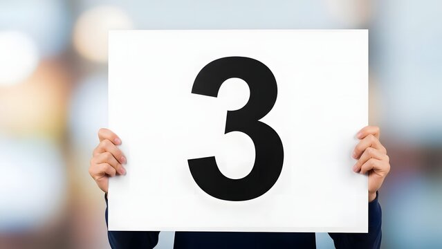 Number 3 printed on white placard, person holding large digit three sign, countdown or ranking concept on bokeh background