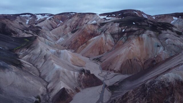 Aerial view of colorful rhyolite mountains with snow patches and winding river beds in Landmannalaugar, Rangarthing ytra, Iceland.