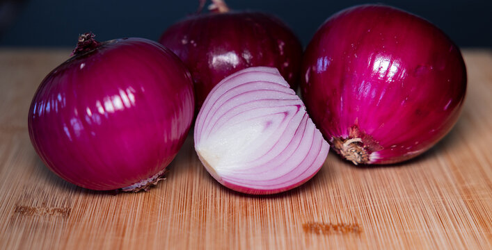 Close-up of three red onions on a cutting board, with half an onion in the foreground. Contains vitamin C and fiber., vegetables, vegatarian food, healthy lifestyle, fresh, raw food.