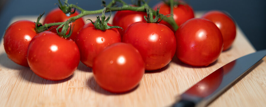 Ripe vine tomatoes with their stems still attached, on a cutting board, next to a kitchen knife. Freshness, vegetable, contains vitamin C, potassium. Healthy eating, healthy lifestyle, raw food.