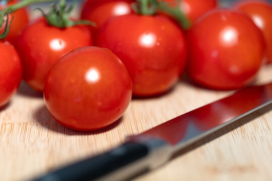 Close-up ripe tomatoes with their stems still attached, on a cutting board, next to a kitchen knife. Freshness, vegetable, contains vitamin C, potassium. Healthy eating, healthy lifestyle, raw food.