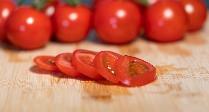 A sliced ripe tomato on a cutting board, with more tomatoes in the background. Freshness, vegetable, contains vitamin C, potassium. Healthy eating, healthy lifestyle, raw food.