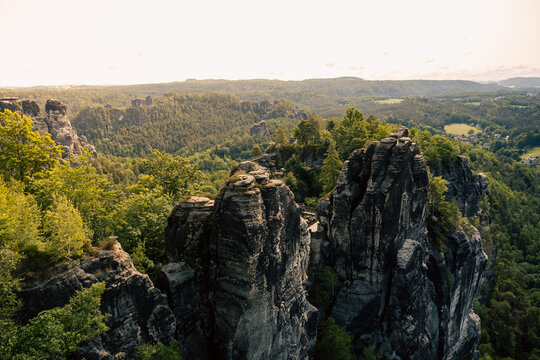 Spektakul&auml;re Aussicht auf die markanten Sandsteinfelsen der Bastei in der S&auml;chsischen Schweiz mit dichtem gr&uuml;nen Wald unter warmem Sonnenlicht.