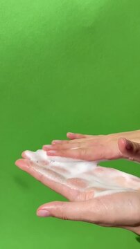 Close up of female hands applying facial cleansing foam, washing face skincare routine, beauty self care concept on green background. Facial cleanser application content, vertical lifestyle ugc video
