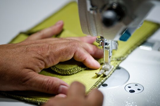 Close-up of tailor hands guiding cloth under overlock machine at sewing factory, clothing production and manufacturing, high resolution Photo