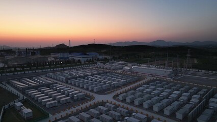 Fototapeta premium Large-scale energy storage power station at sunset with orderly battery arrays and mountain backdrop