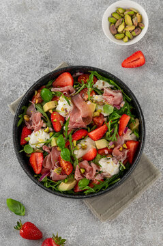 Salad with strawberries, tomatoes, avocado, jamon, burrata and pistachios in a bowl. Fresh summer salad. Top view.