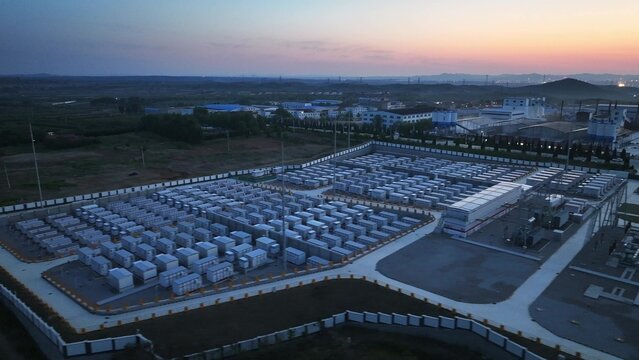 Large-scale energy storage station captured at dusk with aerial view showing modular battery arrays and industrial facility layout