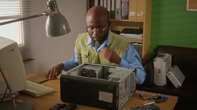 African American man repairing retro desktop computer tower at workshop desk. Clip is perfect for IT support services, hardware repair training, and vintage technology marketing