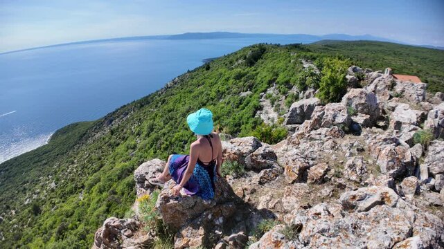 Woman on cliff enjoying panoramic view of sparkling Adriatic Sea and the Sveti Ivan Beach below. Exploring beautiful nature of Cres Island in Croatia. starting point to Sveti Ivan or Lubenice Beach