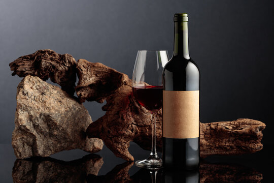 Red wine with old driftwood and a piece of granite rock on a black reflective background.