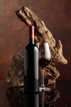 Glass and bottle of red wine with old wooden snag and a piece of granite rock.