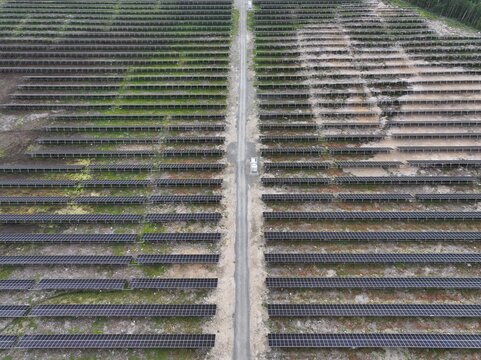 Aerial view of a large solar farm with rows of photovoltaic panels arranged in neat lines separated by a central gravel access road in Utajarvi, North Ostrobothnia, Finland.