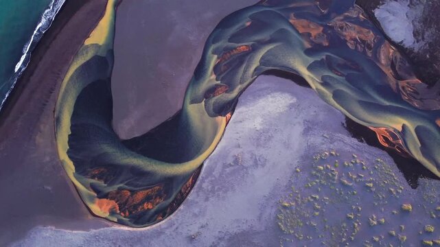 Aerial view of sinuous braided river channels flowing through dark volcanic sand in Iceland.