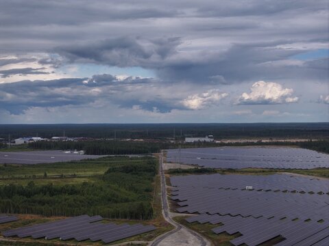 Aerial view of a large solar farm with rows of photovoltaic panels set amidst a vast forest landscape under a dramatic cloudy sky in Utajarvi, North Ostrobothnia, Finland.