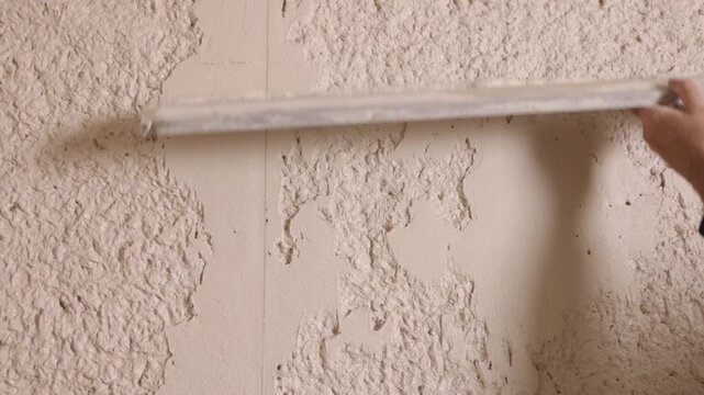 Machine plastering, Construction work, Plaster tools. Close-up worker's hands using long straightedge to level fresh plaster on interior wall during renovation finishing.