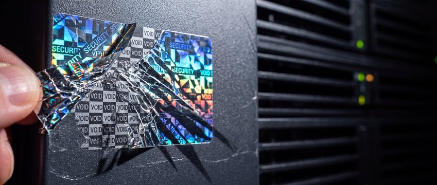 Hand peeling holographic security sticker showing void message from black server hardware to indicate tamper evidence and breach.