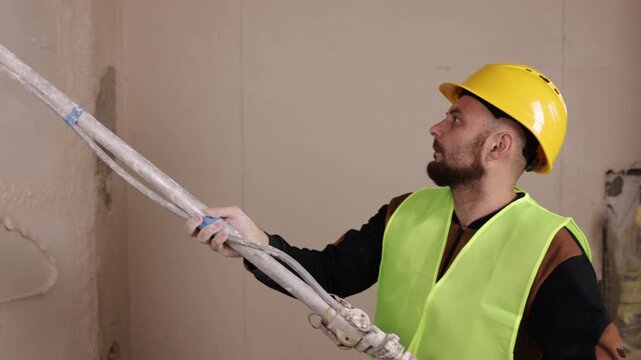 Cement plaster, masonry repair, wall plastering. Hard-hat worker sprays mortar onto block wall to create smooth, finished base layer.