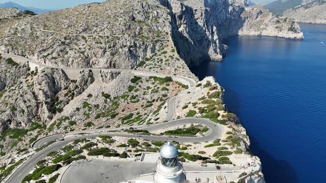Aerial view moving backward revealing Cap de Formentor lighthouse and winding coastal road in Mallorca