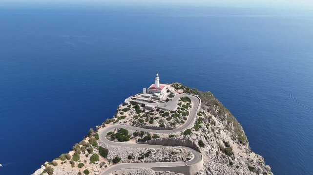 Aerial backward reveal shot pulling away from Cap de Formentor lighthouse perched on dramatic cliffs in Mallorca