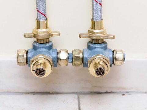 Pair of quarter turn angle stop valves located under a wall with braided supply lines connected in a residential setting