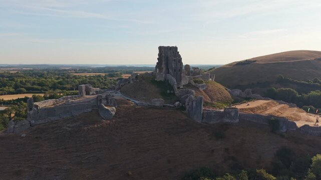 Aerial drone footage of the iconic Corfe Castle in Dorset, England, showcasing the medieval castle ruins, historic village, and rolling Purbeck countryside on a hot summer morning