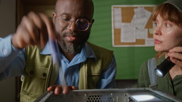 African American man using screwdriver and Caucasian young adult woman holding flashlight to repair computer. Video is ideal for IT support and tech education commercials