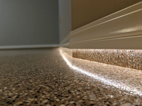 A corner of a residential space features an epoxy-coated garage floor complemented by a baseboard and illuminated by raking light