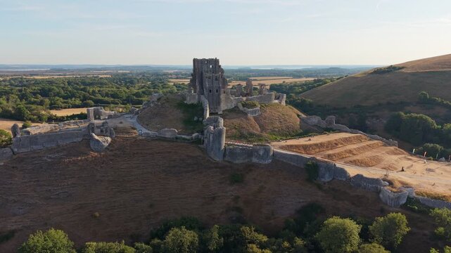 Aerial drone footage of the iconic Corfe Castle in Dorset, England, showcasing the medieval castle ruins, historic village, and rolling Purbeck countryside on a hot summer morning