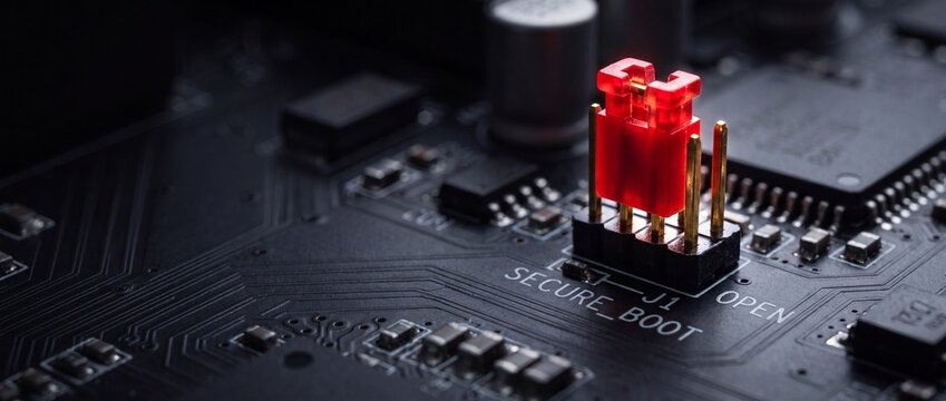 Motherboard circuit board with glowing red secure boot jumper pin on black printed circuit board surface for hardware security.