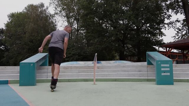 A mature man riding backwards down concrete stairs on aggressive inline skates at an outdoor skatepark