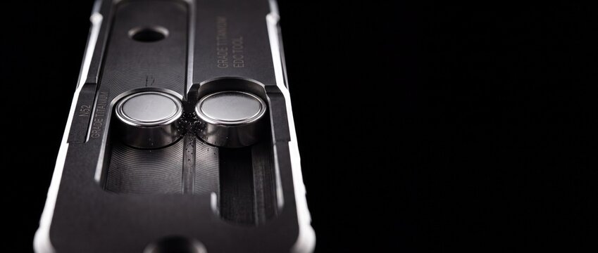 Precision machined titanium edc tool showing small button battery compartments and n52 neodymium magnet details on black backdrop.