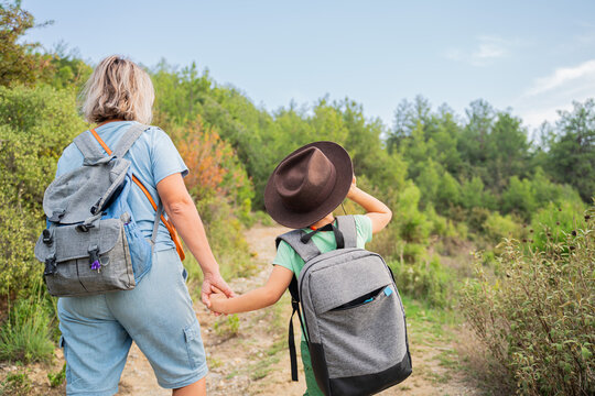 mother and son with backpacks holding hands hiking on forest trail back view
