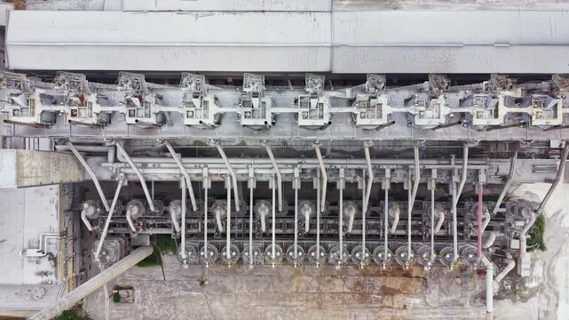 The scene shows a top view of large industrial machines in a factory. Several pipes connect different sections of the equipment. This is a working environment focused on manufacturing processes.
