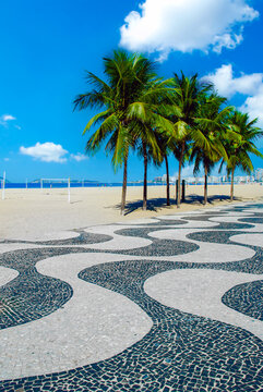 Famous Copacabana beach promenade in Rio de Janeiro with its iconic wave mosaic pavement, tropical palm trees, and sunny blue sky.