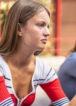 Pensive gen z woman listens during a serious outdoor conversation in a close-up side profile. Natural expression conveys concern, reflection, empathy, and emotional wellbeing.