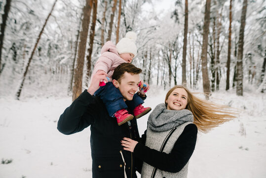 Smiling young family happily spending winter day in snowy forest, father carrying little daughter on shoulders. Happy family leisure and emotions. Closeup.
