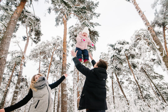 Father cheerfully tossing his little daughter up while the happy mother watches the game joyfully during a winter walk in the forest. Family winter fun outdoors. Closeup.