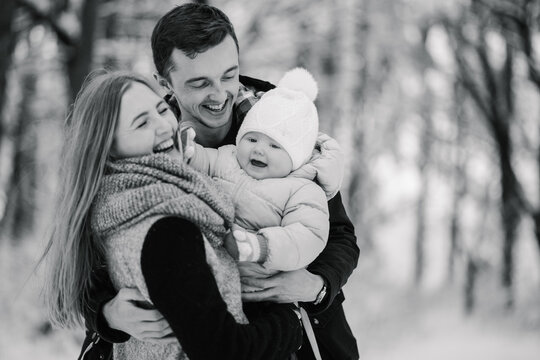 Happy parents laughing, gently hugging little daughter during winter walk. Family joy and love in snowy forest. Black and white photo.
