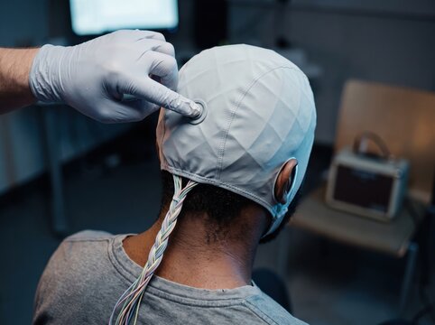 Man wearing EEG cap while researcher adjusts sensor, brain research