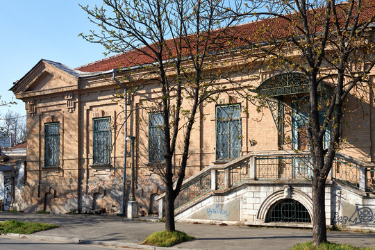Historic brick building with ornate staircase entrance and trees casting shadows