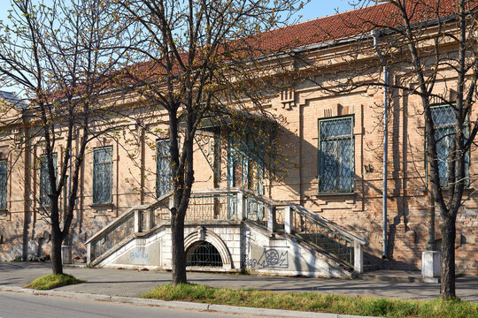 Historic brick building with ornate staircase entrance and trees casting shadows