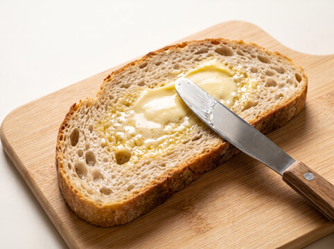 Spreading butter with a knife on a slice of fresh sourdough bread