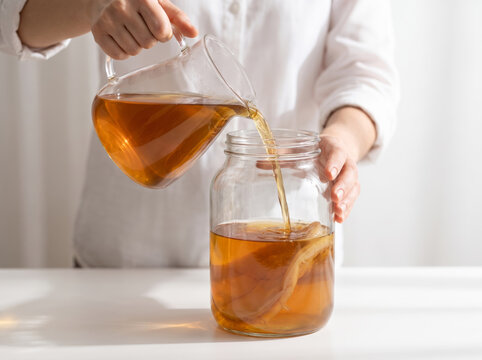 Pouring tea into a glass jar with kombucha SCOBY for fermentation
