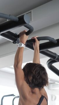 Muscular woman doing pull ups on a horizontal bar during a strength training session, showcasing her strong back muscles and determination while exercising in a modern fitness center