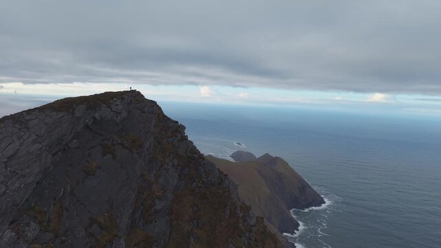 Tiny figure of solo hiker on top of steep Croaghaun mountain cliffs looking at Atlantic Ocean, Achill Island