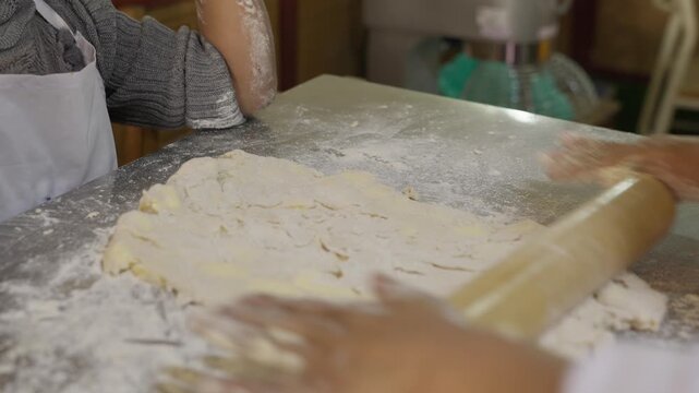 Detail of a girl's hands kneading dough with a rolling pin, stretching and flattening the dough on a table