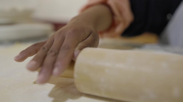 Detail of a girl's hands kneading dough with a rolling pin, stretching and flattening the dough on a table